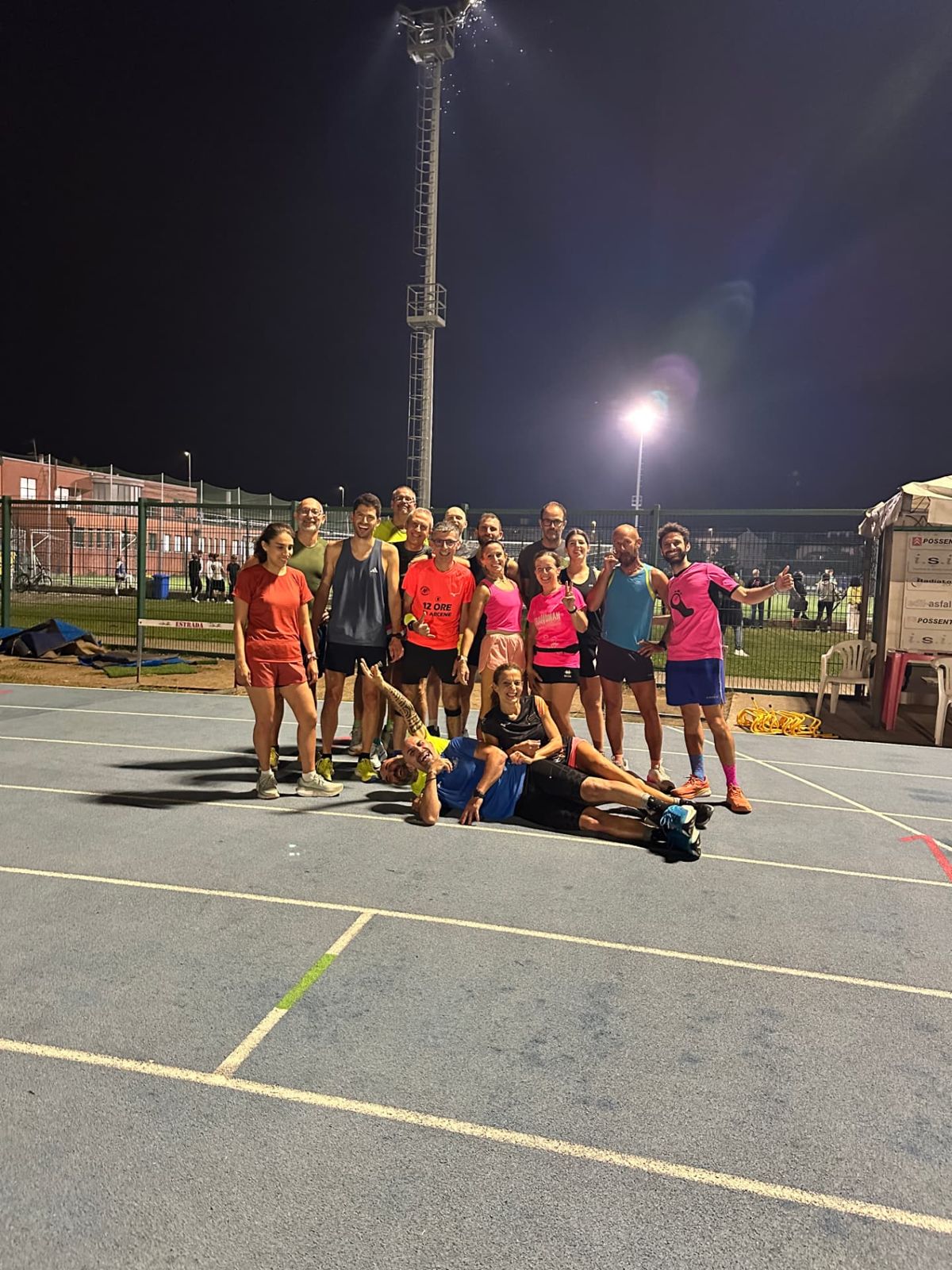 Foto di gruppo del team Let's Run sulla pista di atletica illuminata di sera