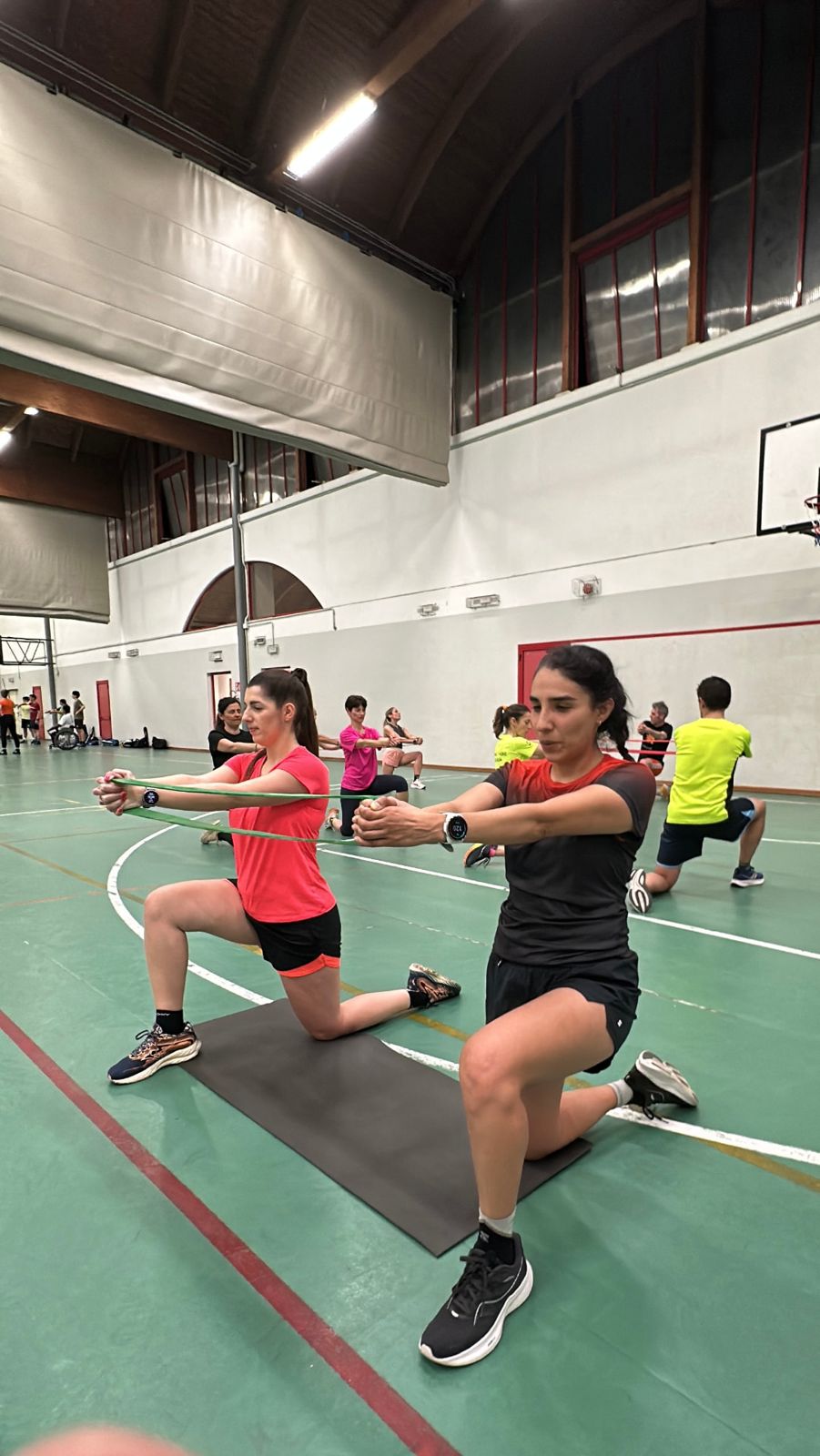 Due atlete eseguono affondi con elastico durante l'allenamento di forza in palestra